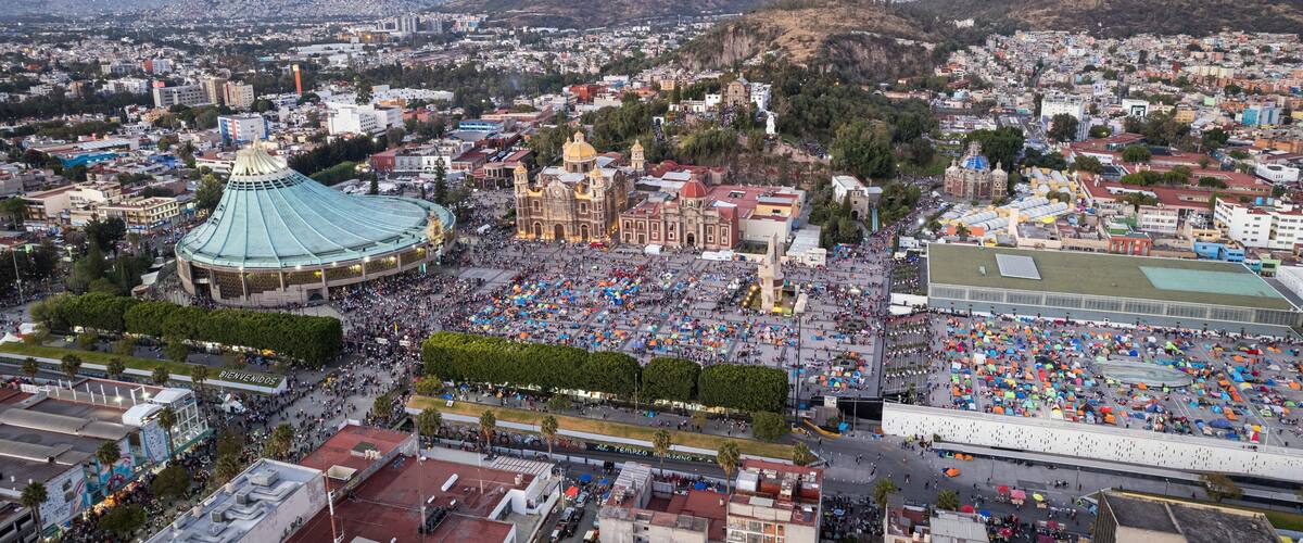 A cityscape with a large stadium, historic buildings, and a mountainous backdrop.