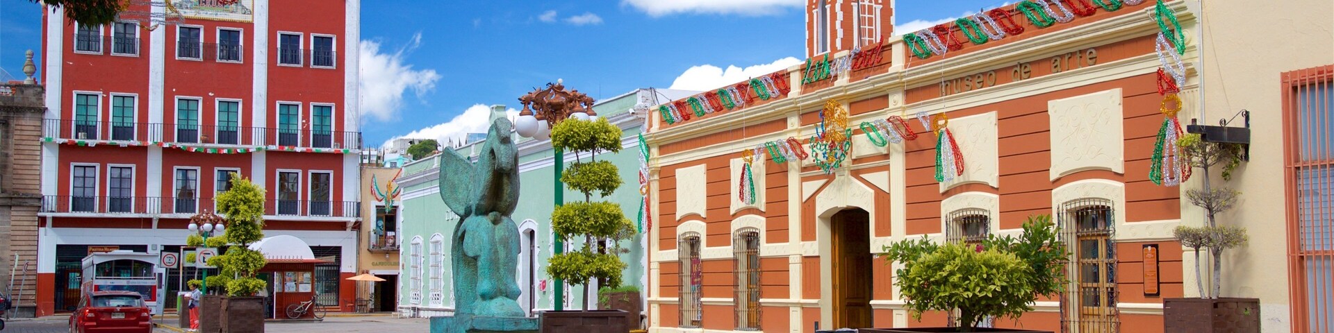 Uma rua histórica com edifícios coloridos, uma estátua imponente e um céu azul límpido.