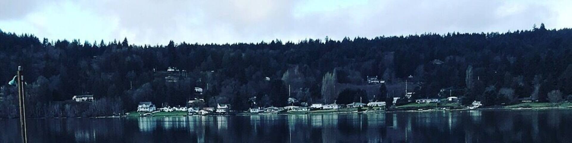 A calm lake with a dock extending into the water, surrounded by a forested hillside.