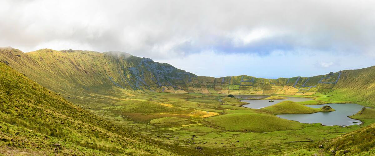 A valley with a lake surrounded by green hills and a cloudy sky.