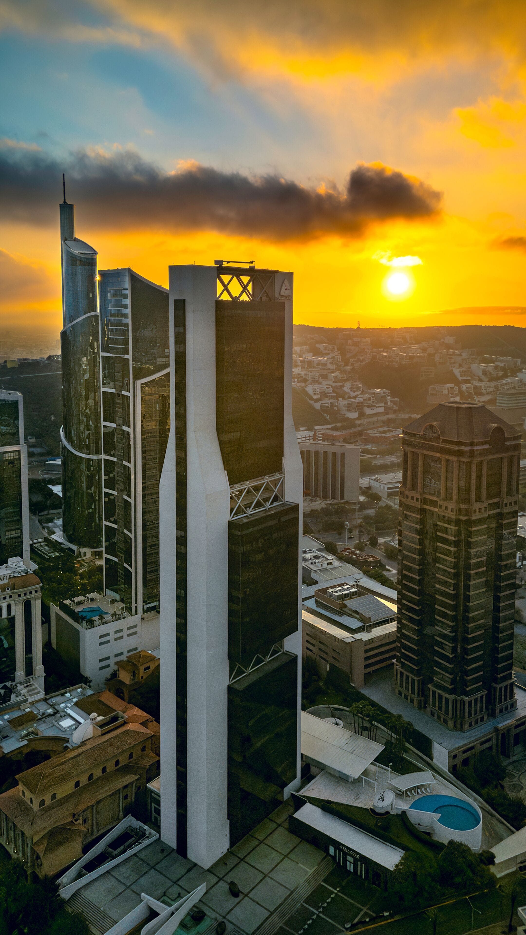 A cityscape with modern skyscrapers, a prominent tower with a unique design, and a sunset in the background.