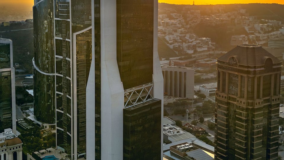 A cityscape with modern skyscrapers, a prominent tower with a unique design, and a sunset in the background.