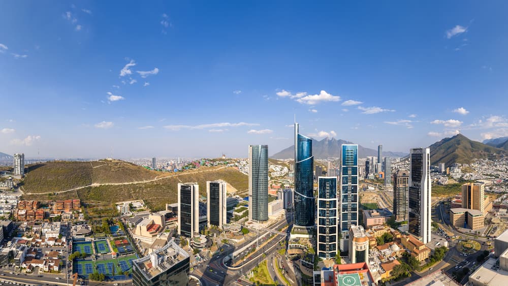 Panoramica urbana con grattacieli moderni, un terreno collinare e un cielo azzurro limpido.