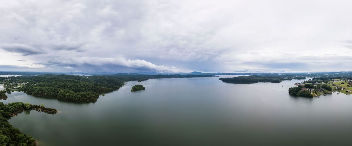 A large lake surrounded by dense forests and small islands, with a cloudy sky above.