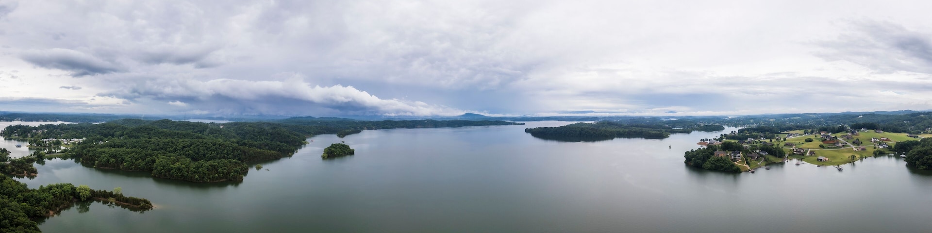 A large lake surrounded by dense forests and small islands, with a cloudy sky above.