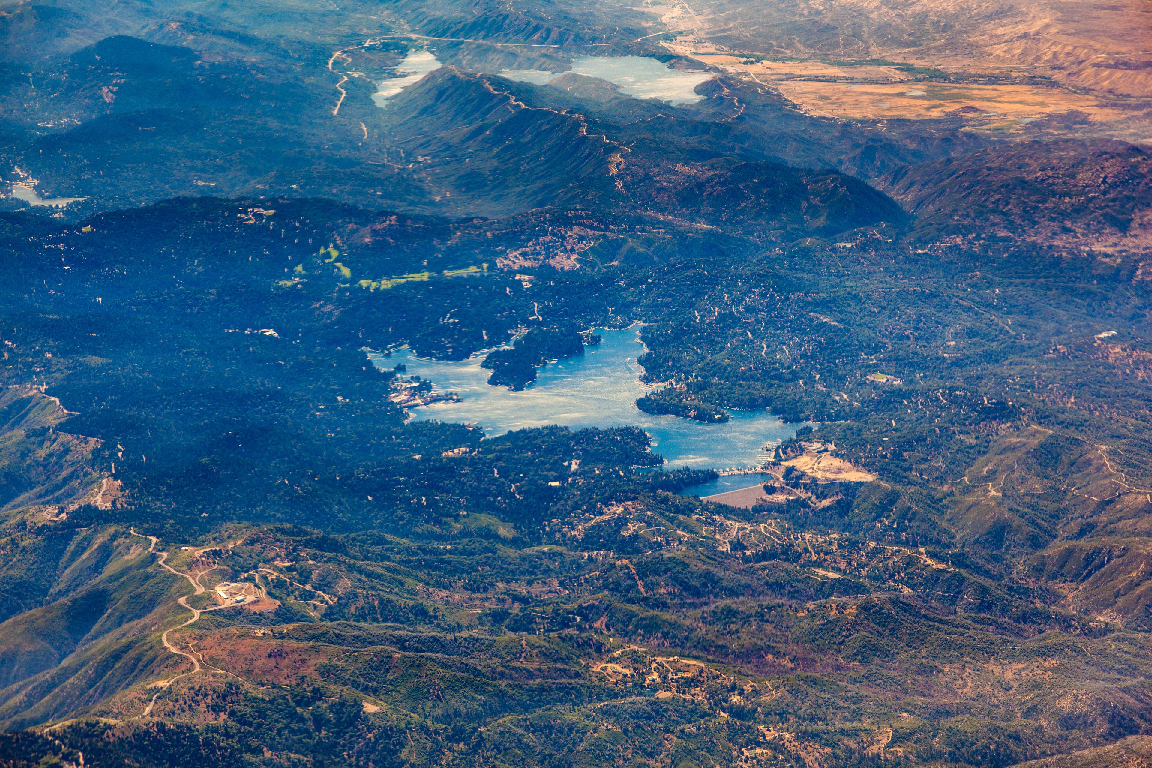 Un paisaje montañoso con un gran lago rodeado de bosques densos y carreteras sinuosas.