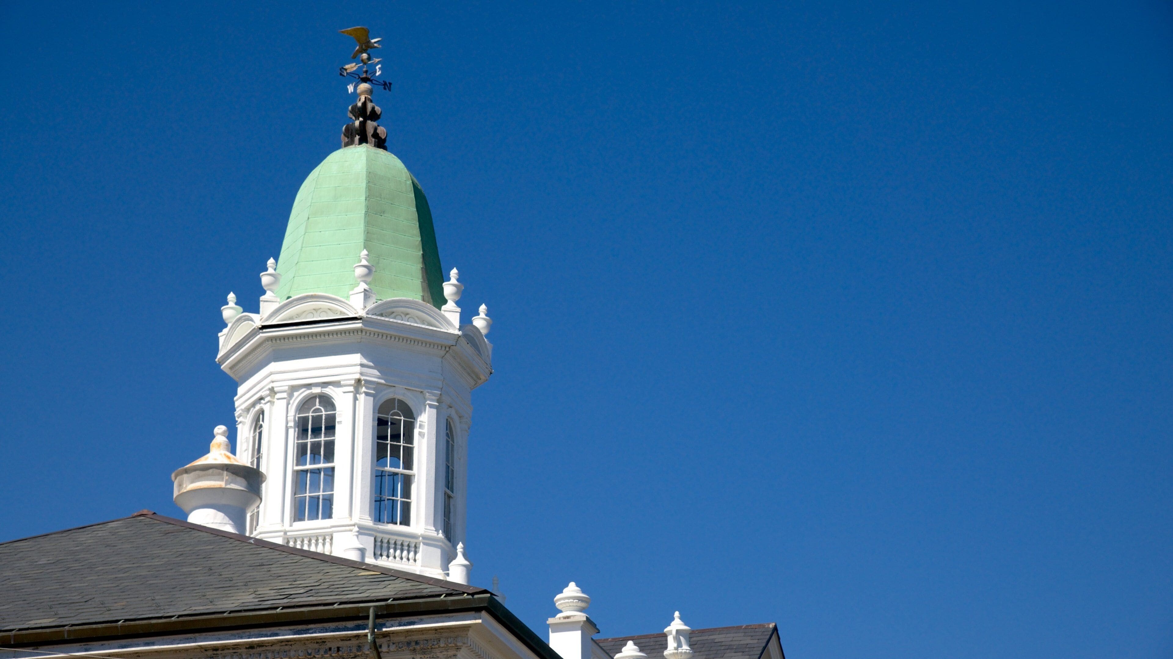 A white building with a green dome and a weather vane on top.