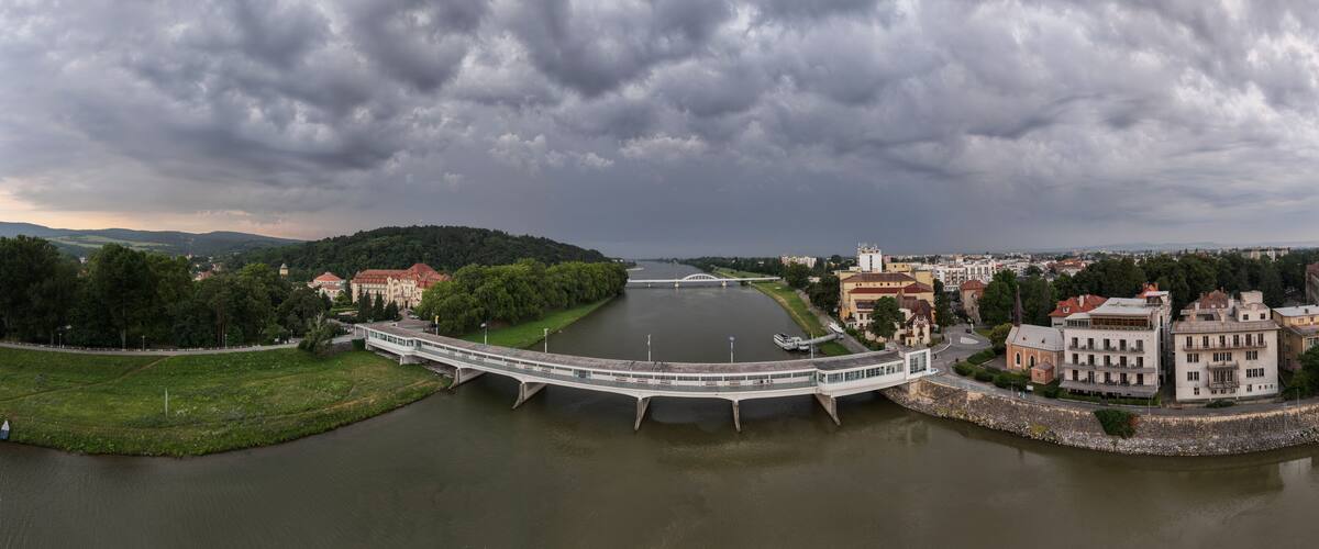 A river with a bridge, a cityscape, and a hill in the background.