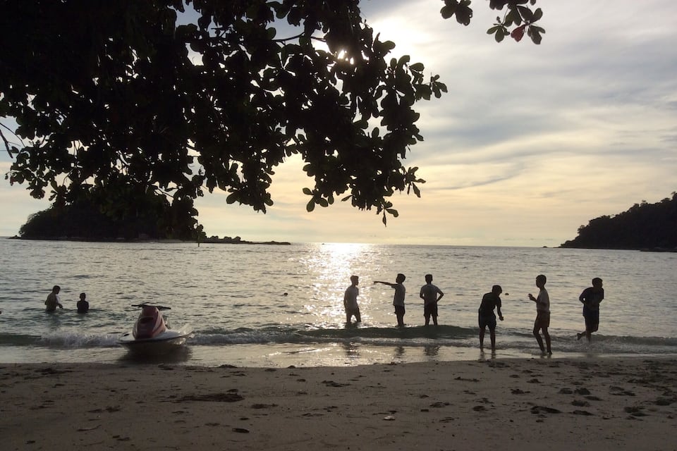 A beach with people playing in the water and a boat.