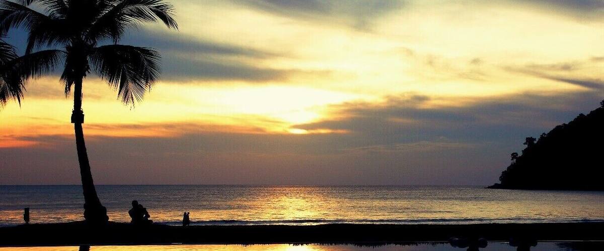 Un atardecer sobre una playa con palmeras y aguas tranquilas que reflejan el cielo.