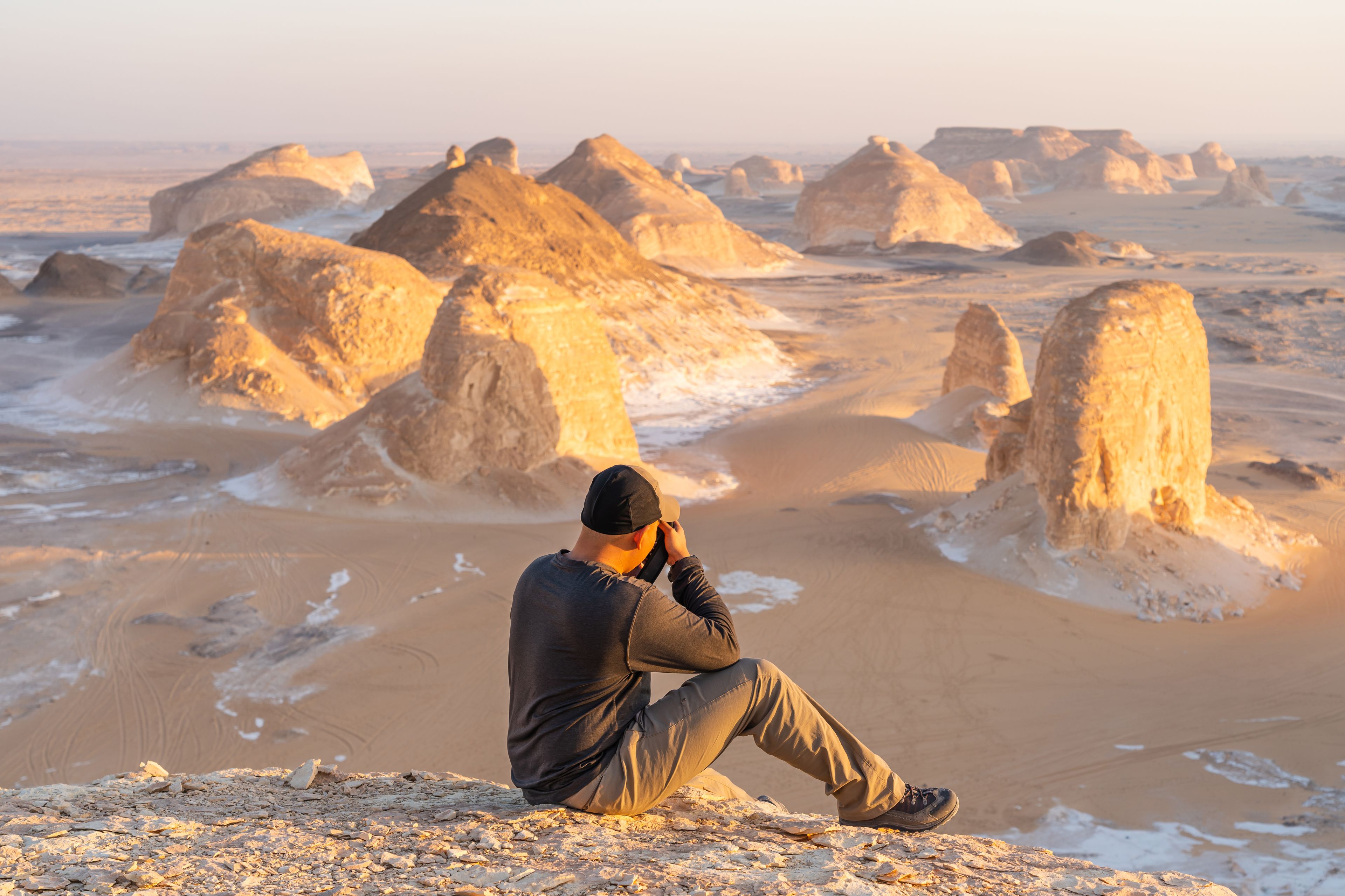 A person sitting on a rocky outcrop overlooking a desert landscape with prominent rock formations.