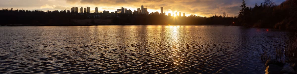 Un coucher de soleil sur les toits d’une ville, dont le reflet se mire dans les eaux calmes.