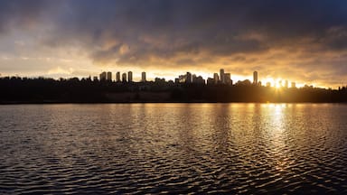 Pôr do sol refletido em águas calmas sobre o horizonte urbano.