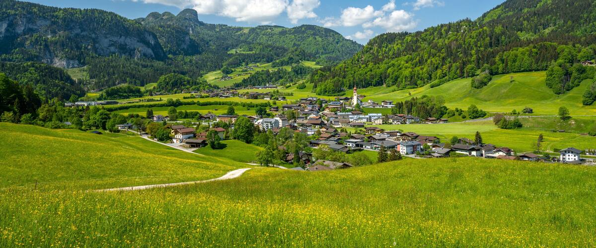 A village nestled in a valley with green fields and mountains in the background.