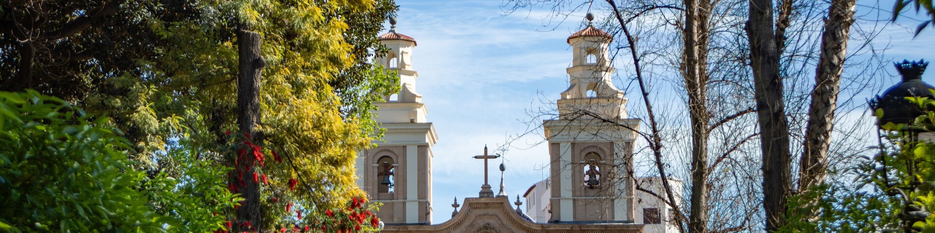 Facade of the baroque church of El Carmen in Murcia, Spain, among the leafy trees of the Floridablanca garden