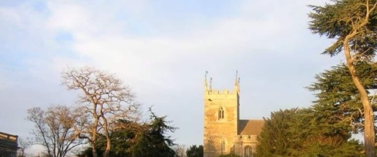 A pathway leading to a historic church with a tall tower, surrounded by well-maintained gardens and trees.