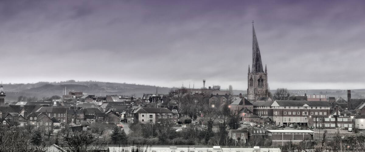 A town with a prominent church spire, residential buildings, and a hill in the background.