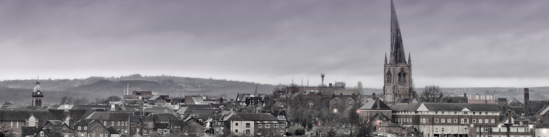 A town with a prominent church spire, residential buildings, and a hill in the background.