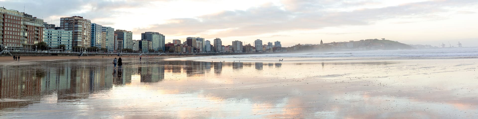 Gijón reflejado en la arena humeda de la playa de San Lorenzo en baja mar . Panorámica de Xixón, Asturias, España.