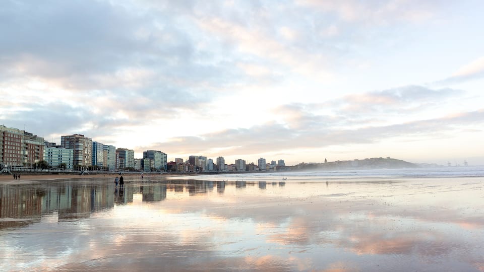Gijón reflejado en la arena humeda de la playa de San Lorenzo en baja mar . Panorámica de Xixón, Asturias, España.