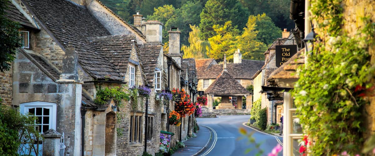 A quaint village street lined with stone buildings, a curved road, and hanging flower baskets.