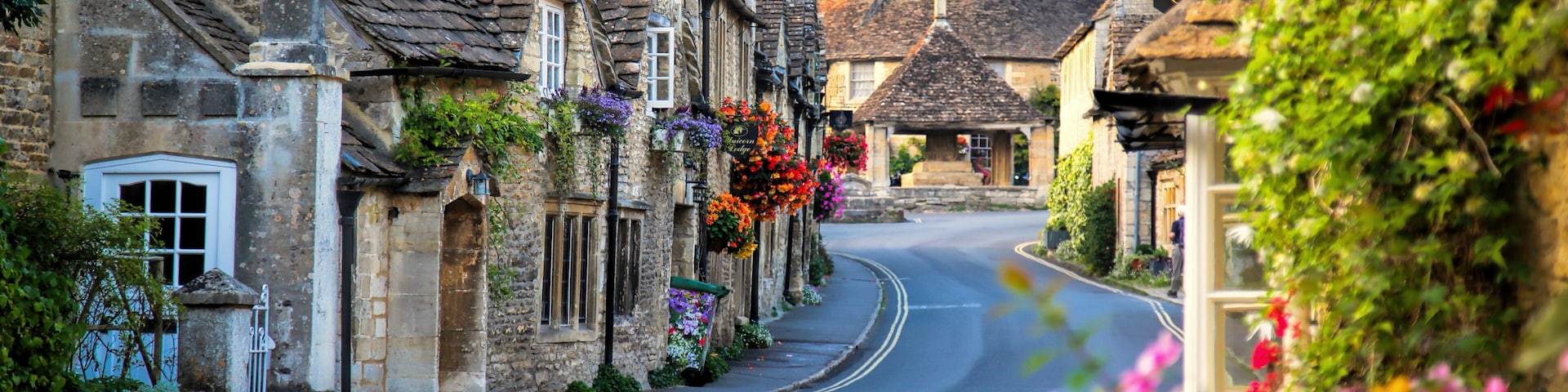 A quaint village street lined with stone buildings, a curved road, and hanging flower baskets.