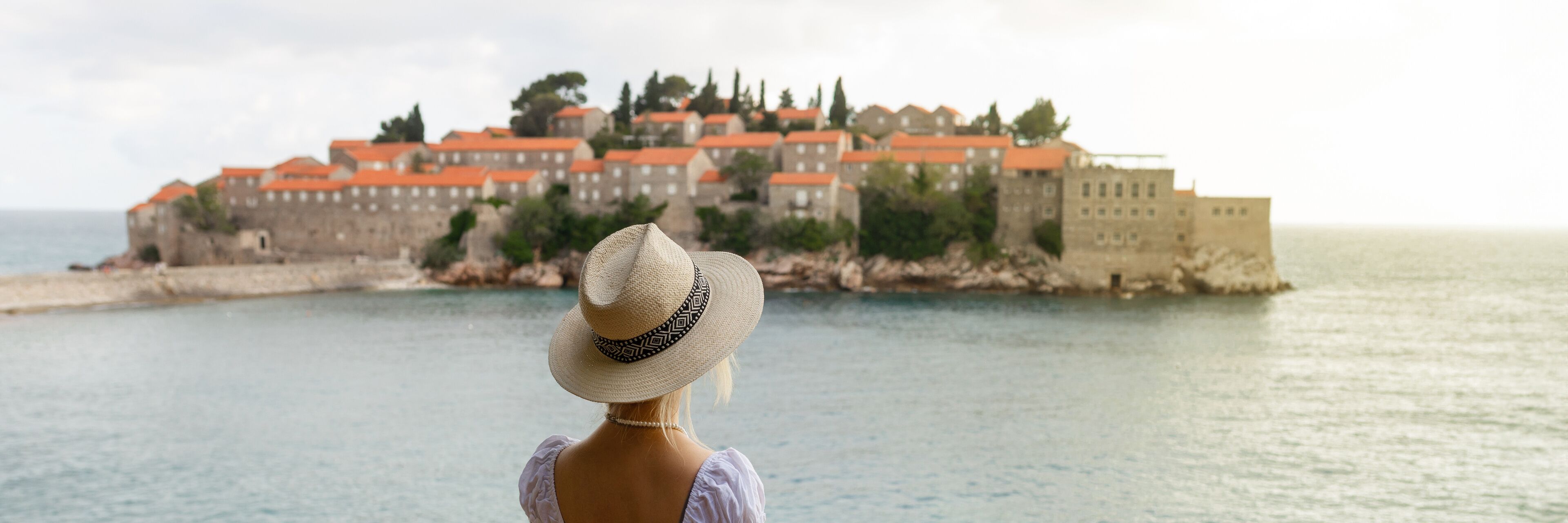 A woman in a straw hat overlooking a coastal town with red-roofed buildings.