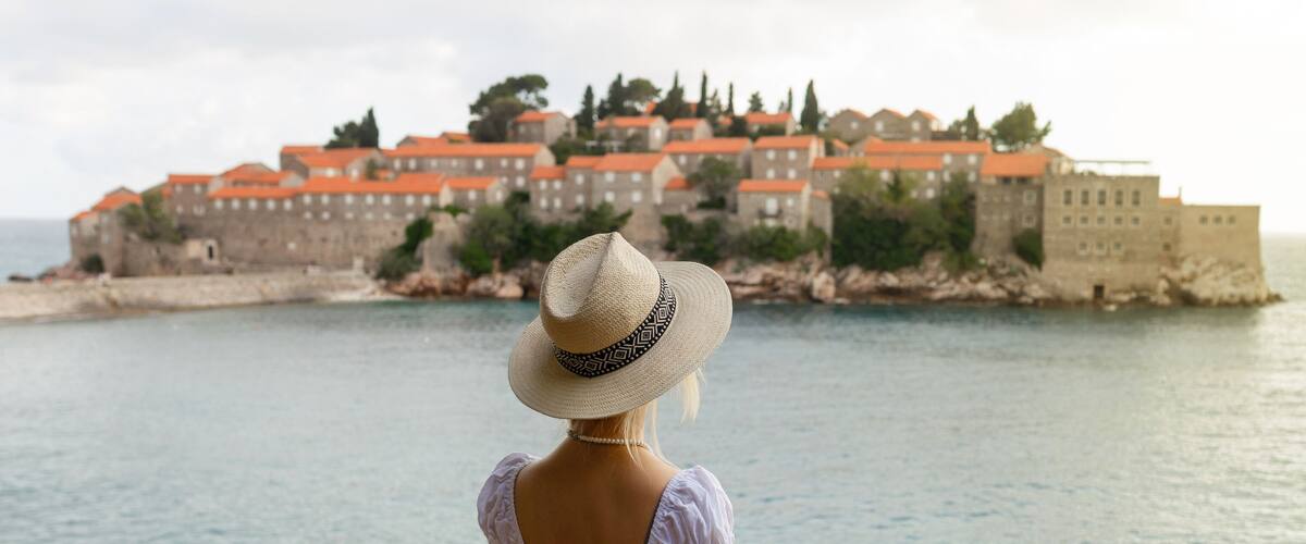 A woman in a straw hat overlooking a coastal town with red-roofed buildings.