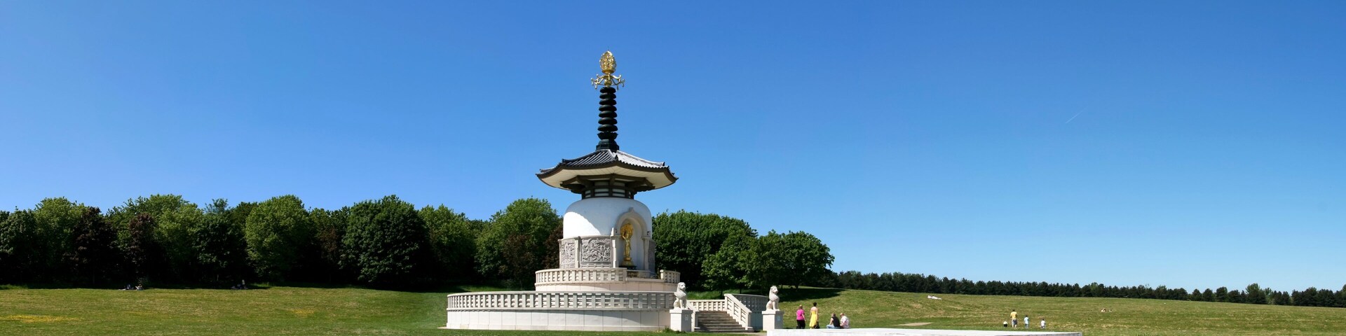 A white pagoda with a golden spire in a grassy field.