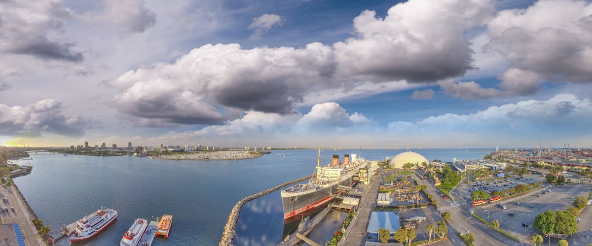 A coastal cityscape with a large body of water, a prominent dome structure, and several ships docked at the port.