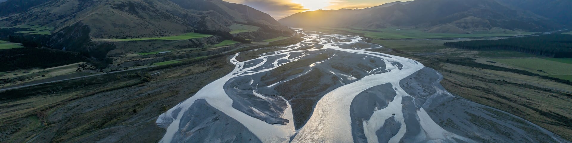A river winding through a mountainous valley with a sunset in the background.