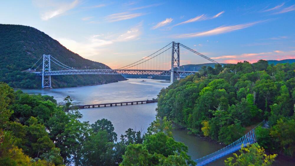 A suspension bridge over a river, surrounded by dense forest and hills.