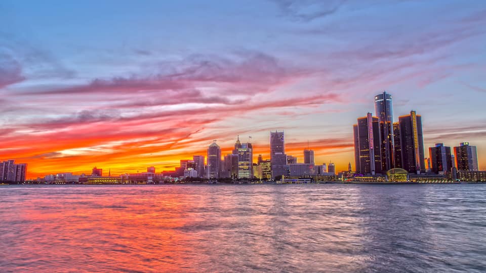 A city skyline at sunset with a river in the foreground.
