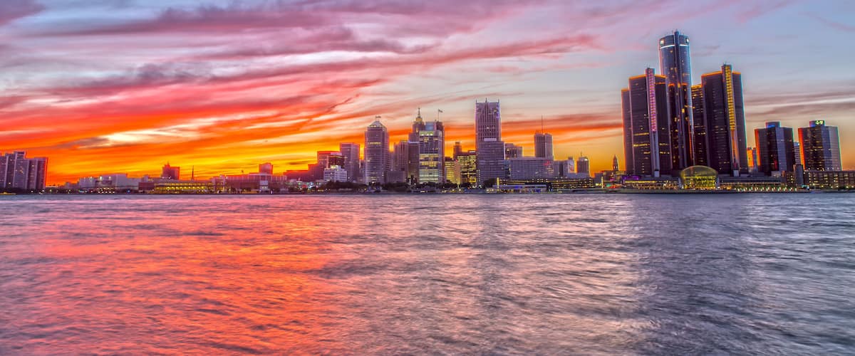 A city skyline at sunset with a river in the foreground.