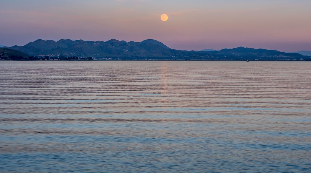 A calm lake with a mountain range in the background and a full moon in the sky.