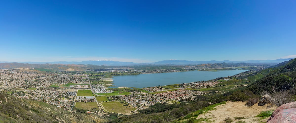 A panoramic view of a coastal city with a large lake, surrounded by hills and mountains.