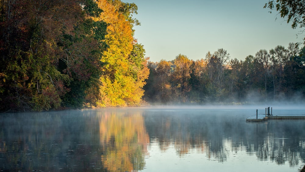A calm lake with autumn foliage and a dock.