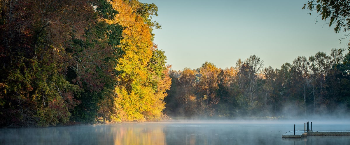 A calm lake with autumn foliage and a dock.