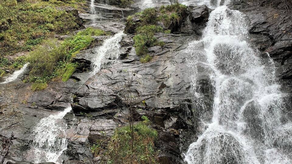 A multi-tiered waterfall cascading over rocky terrain with lush greenery.