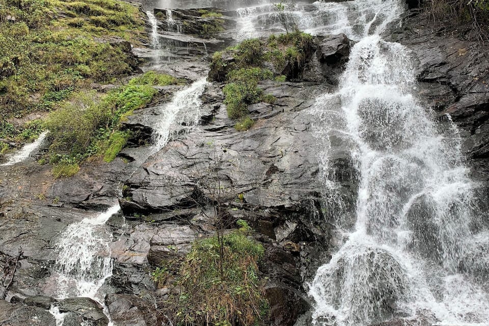 A multi-tiered waterfall cascading over rocky terrain with lush greenery.