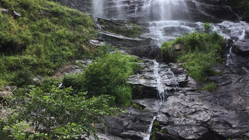 A multi-tiered waterfall cascading over rocky terrain surrounded by lush greenery.