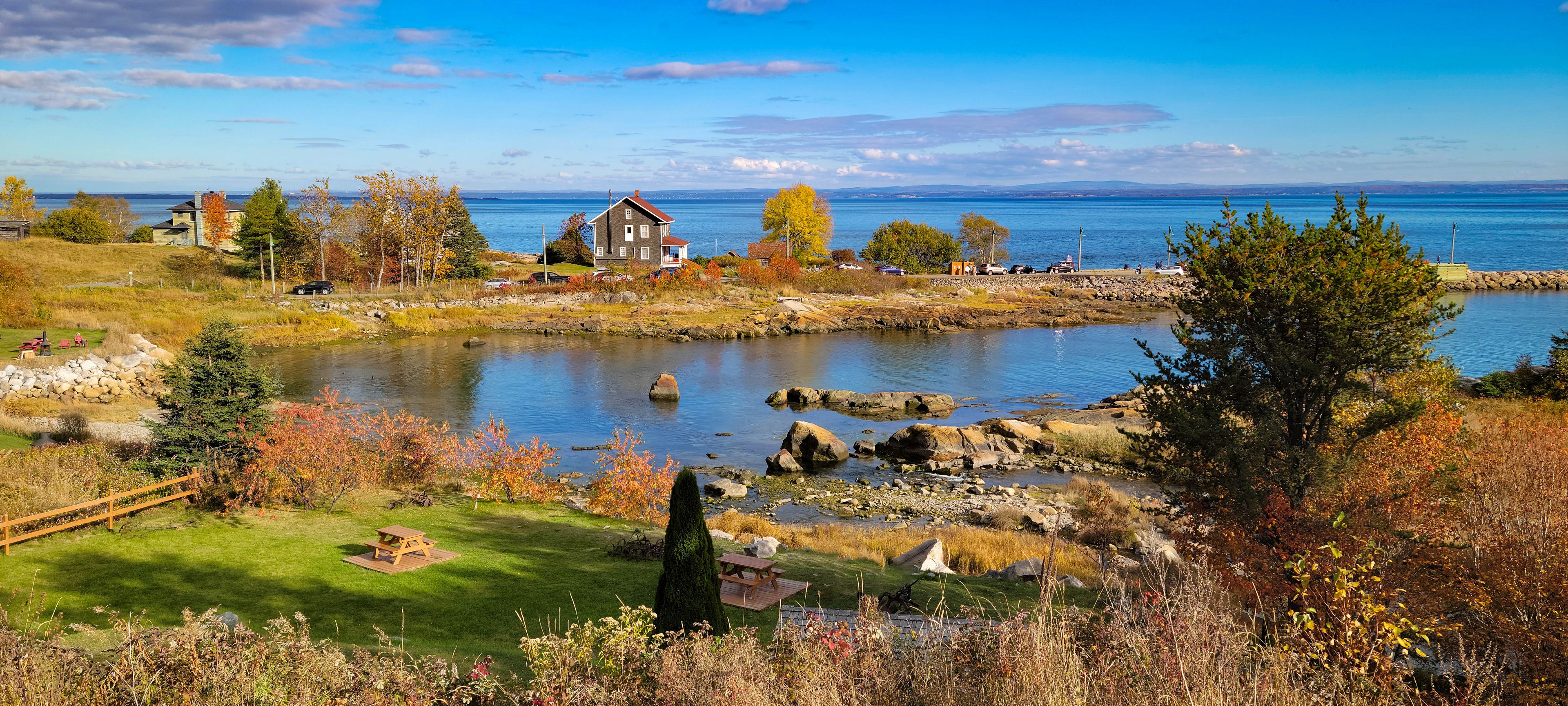 A lakeside landscape with autumn foliage, a stone bridge, and a house with a red roof.