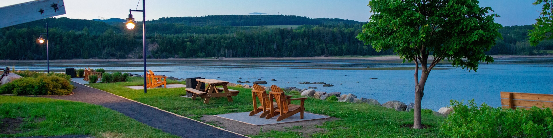 Un parque junto al lago con mesas de picnic, un camino para pasear y un banco.