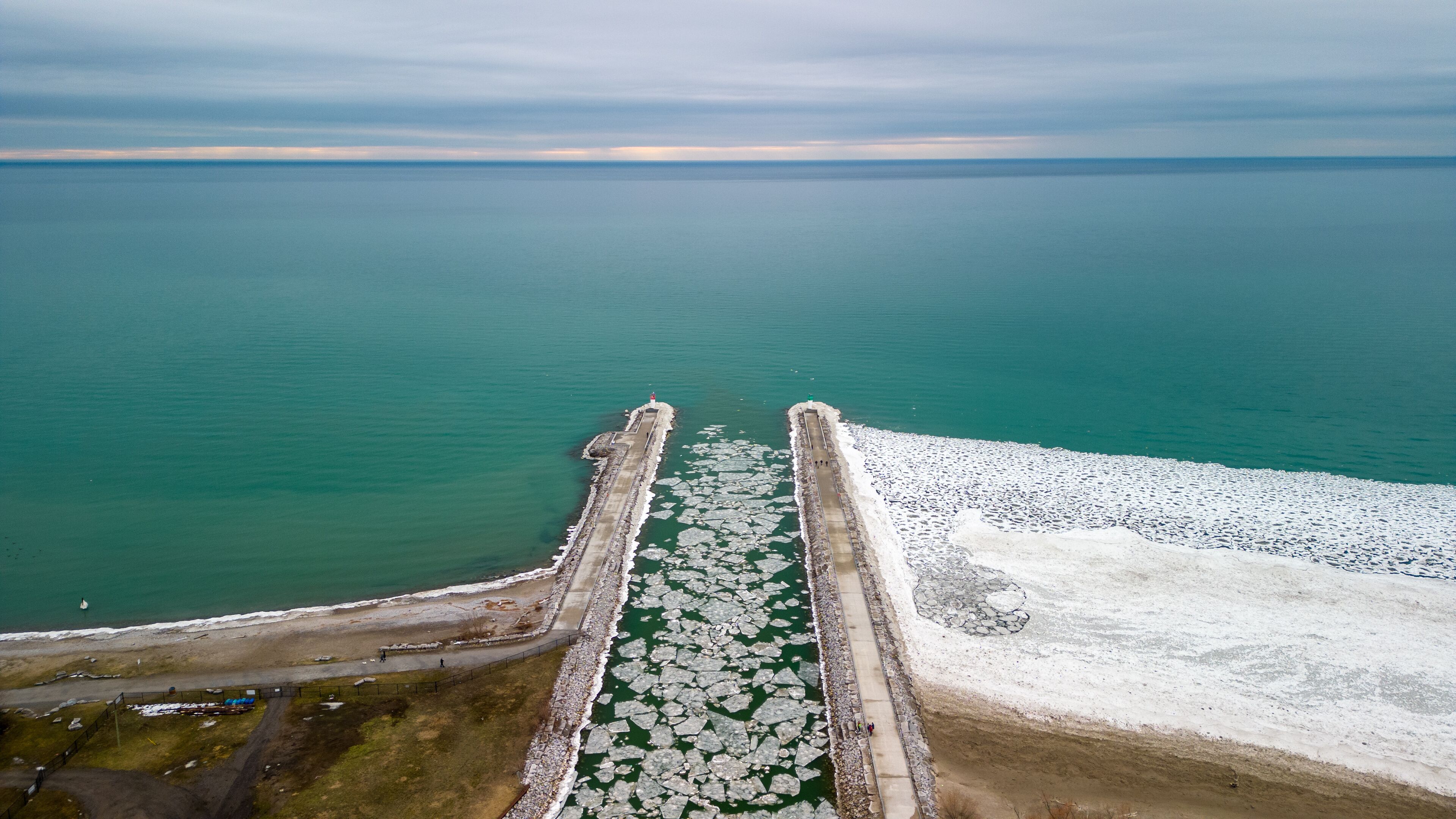A coastal scene with a frozen waterway, a lighthouse, and a rocky shoreline.