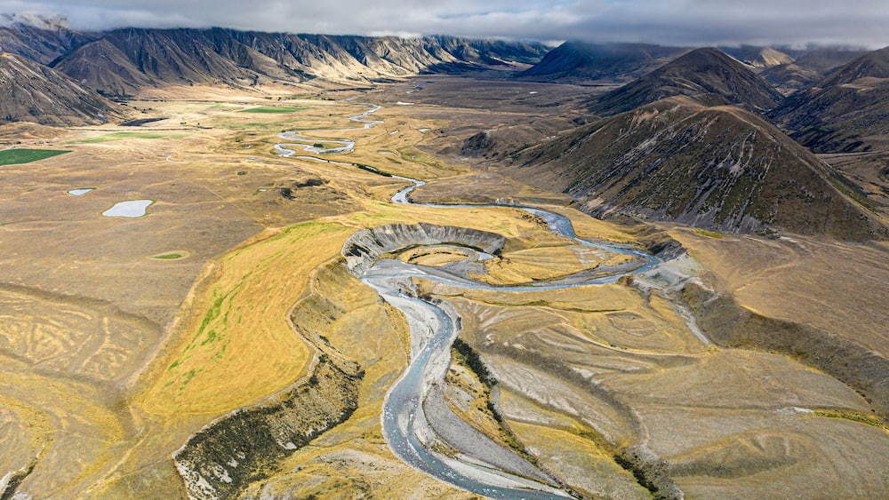 Une rivière sinueuse traverse un paysage montagneux, parsemé de zones de végétation verdoyante et de terrains rocheux.
