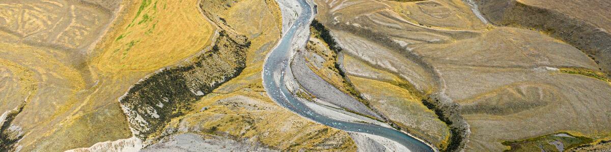 A winding river through a mountainous landscape with patches of green vegetation and rocky terrain.