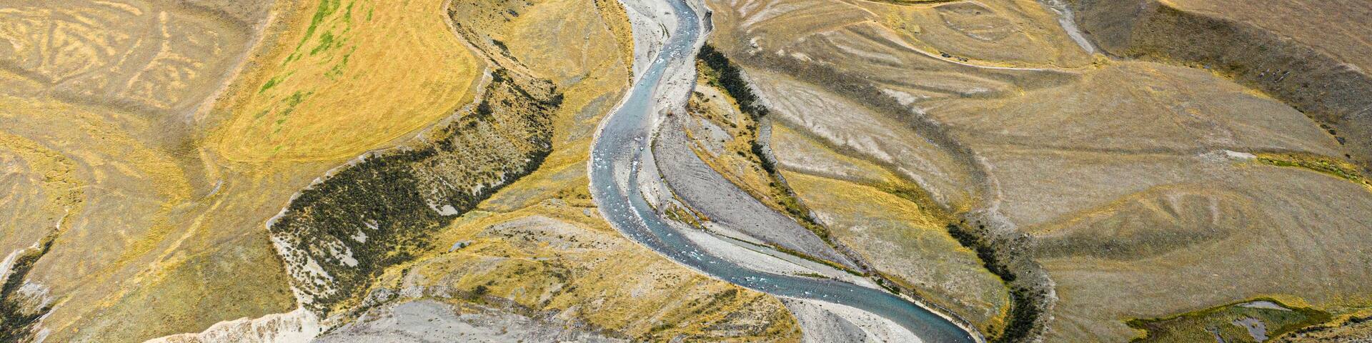 A winding river through a mountainous landscape with patches of green vegetation and rocky terrain.