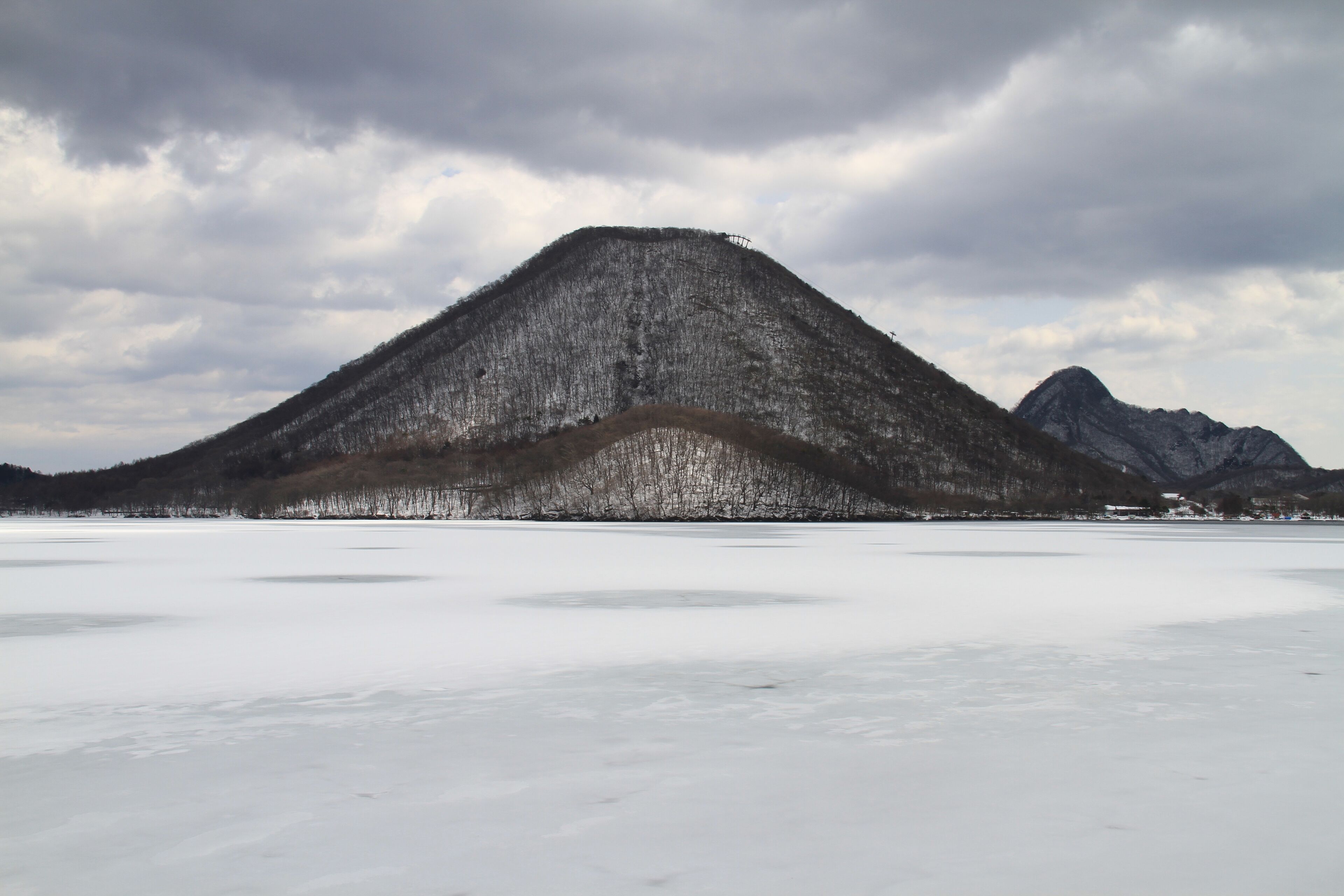 A snow-covered mountain range with a flat, icy foreground.