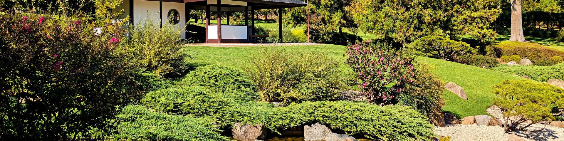 A pavilion with a tiled roof, surrounded by lush greenery and a small stream.