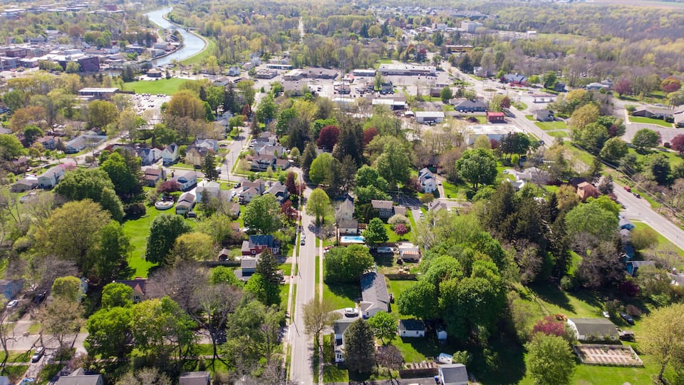 An aerial view of a suburban neighborhood with houses, a river, and a mix of greenery and paved areas.
